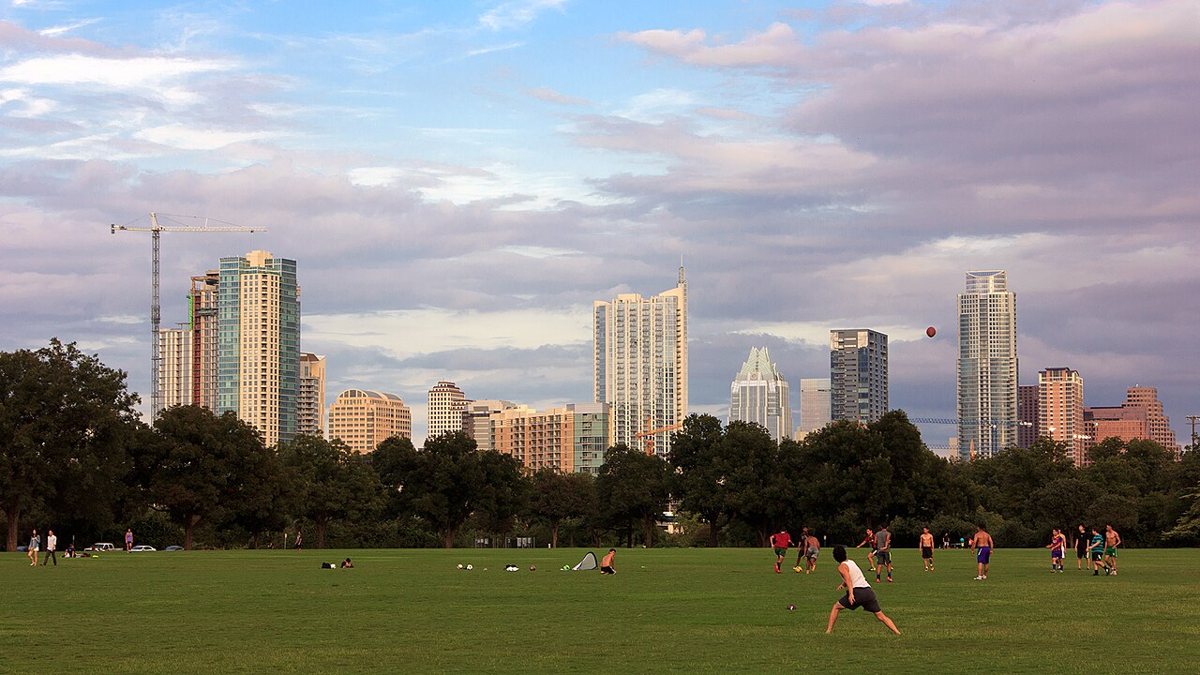 Wide green lawn and tree canopy at Zilker Park with the downtown Austin skyline visible in the distance